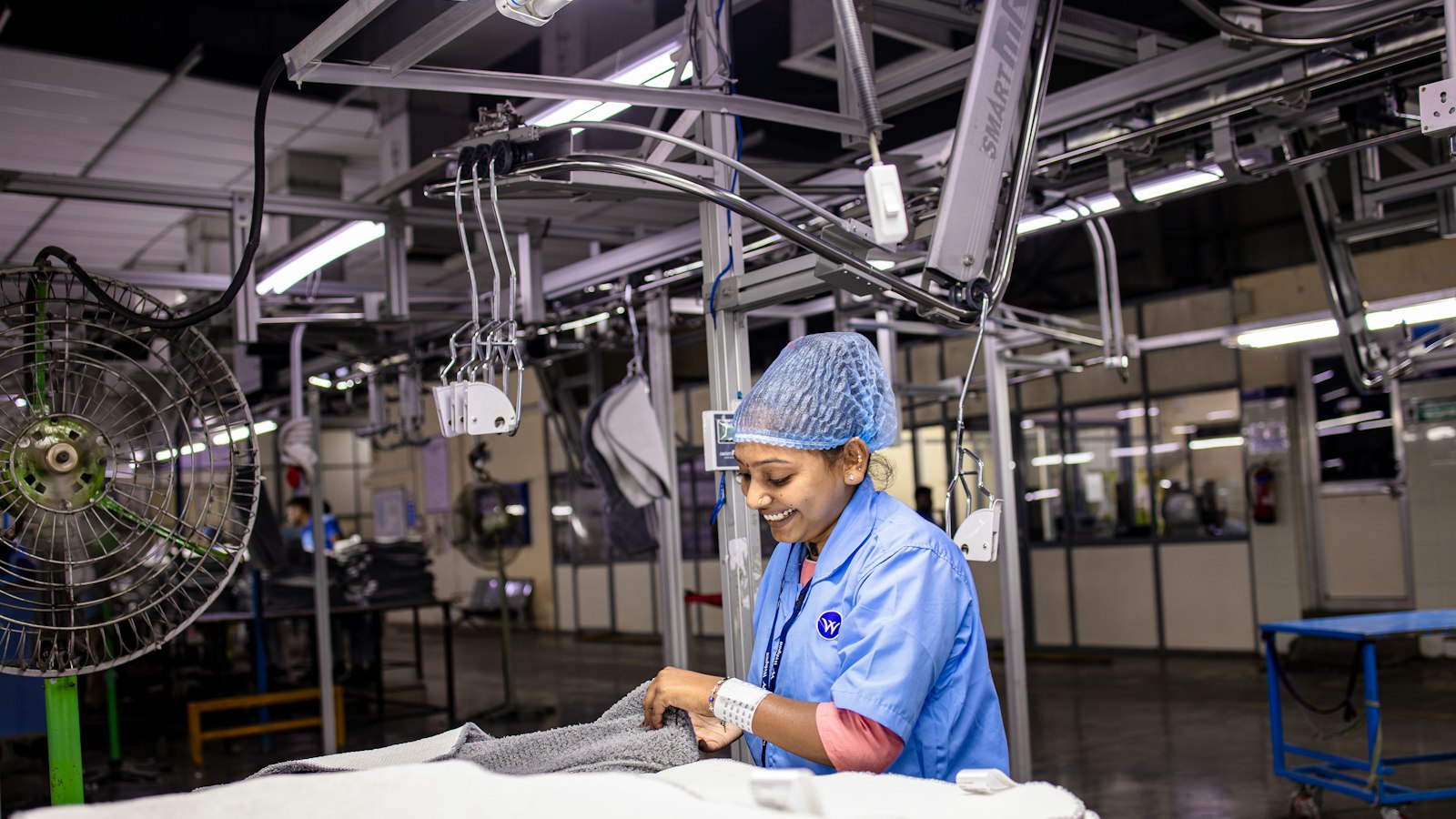 A smiling factory worker in a hairnet inspects fabric on a production line