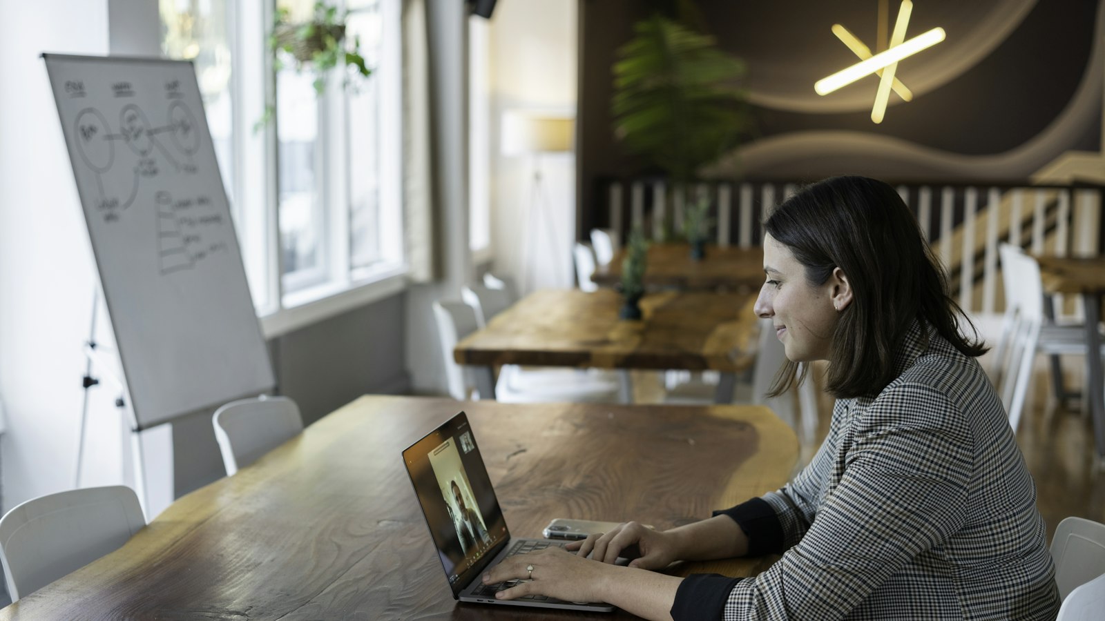 Woman in a plaid blazer on a video call at a laptop in an office