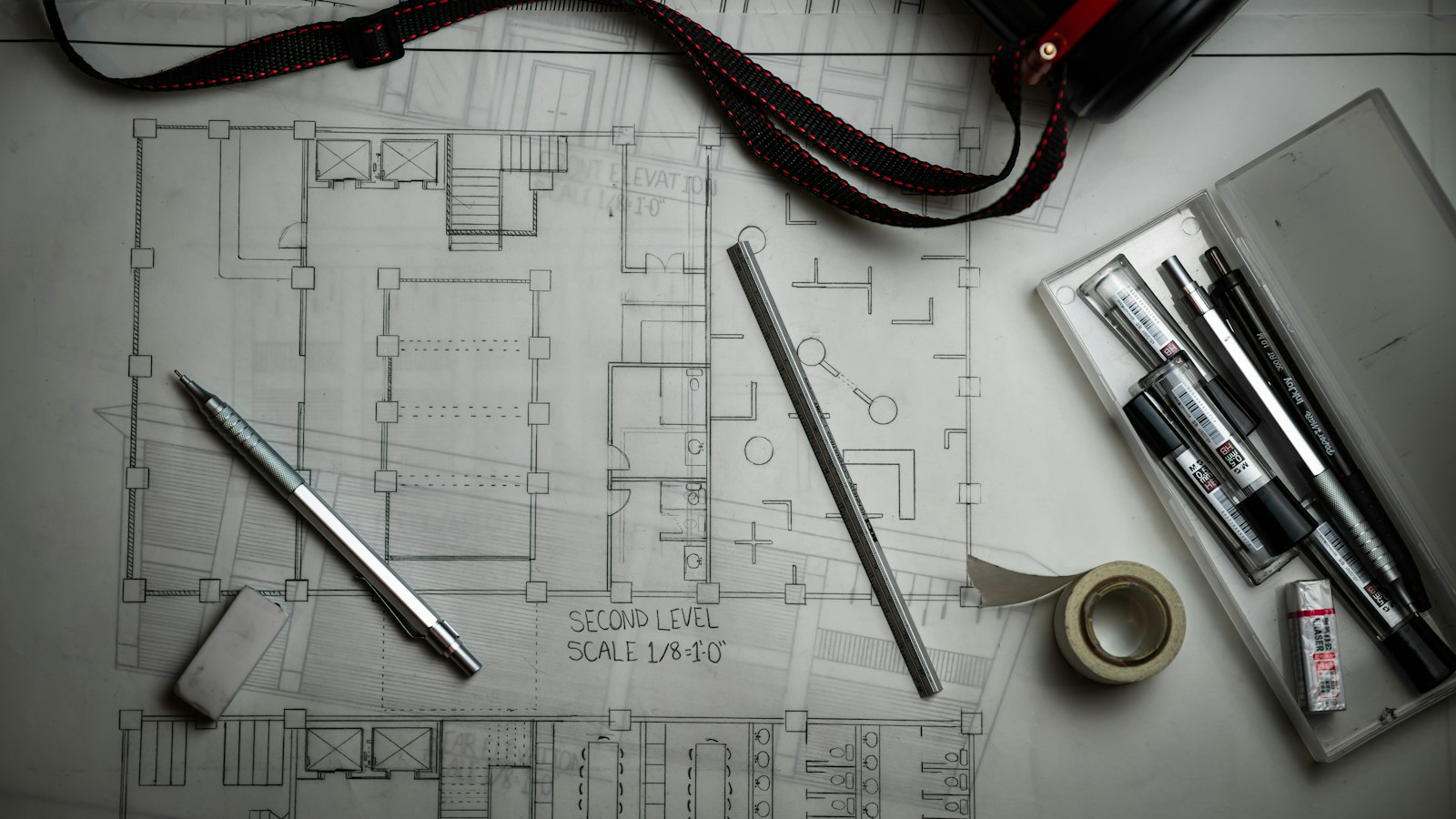 Architectural floor plan blueprints with drafting pencils, a metal ruler and a pen case