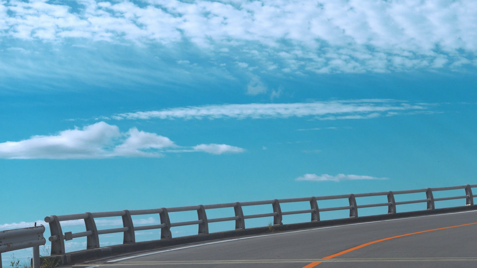 Curved coastal road with a metal guardrail under a bright blue sky