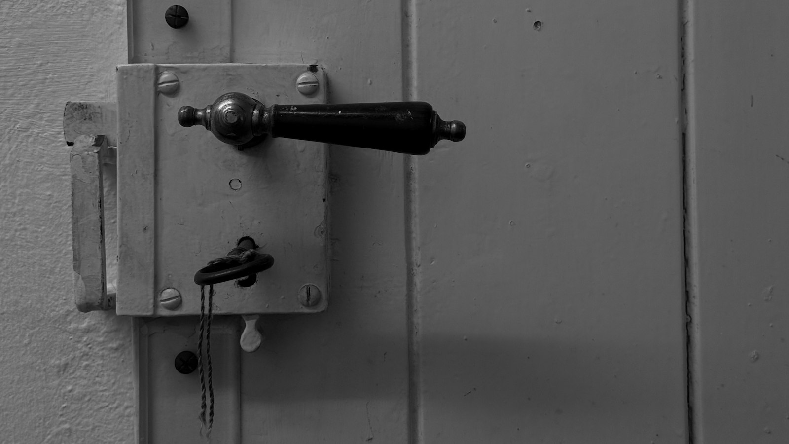 A black and white close up of an old door handle and lock with a key