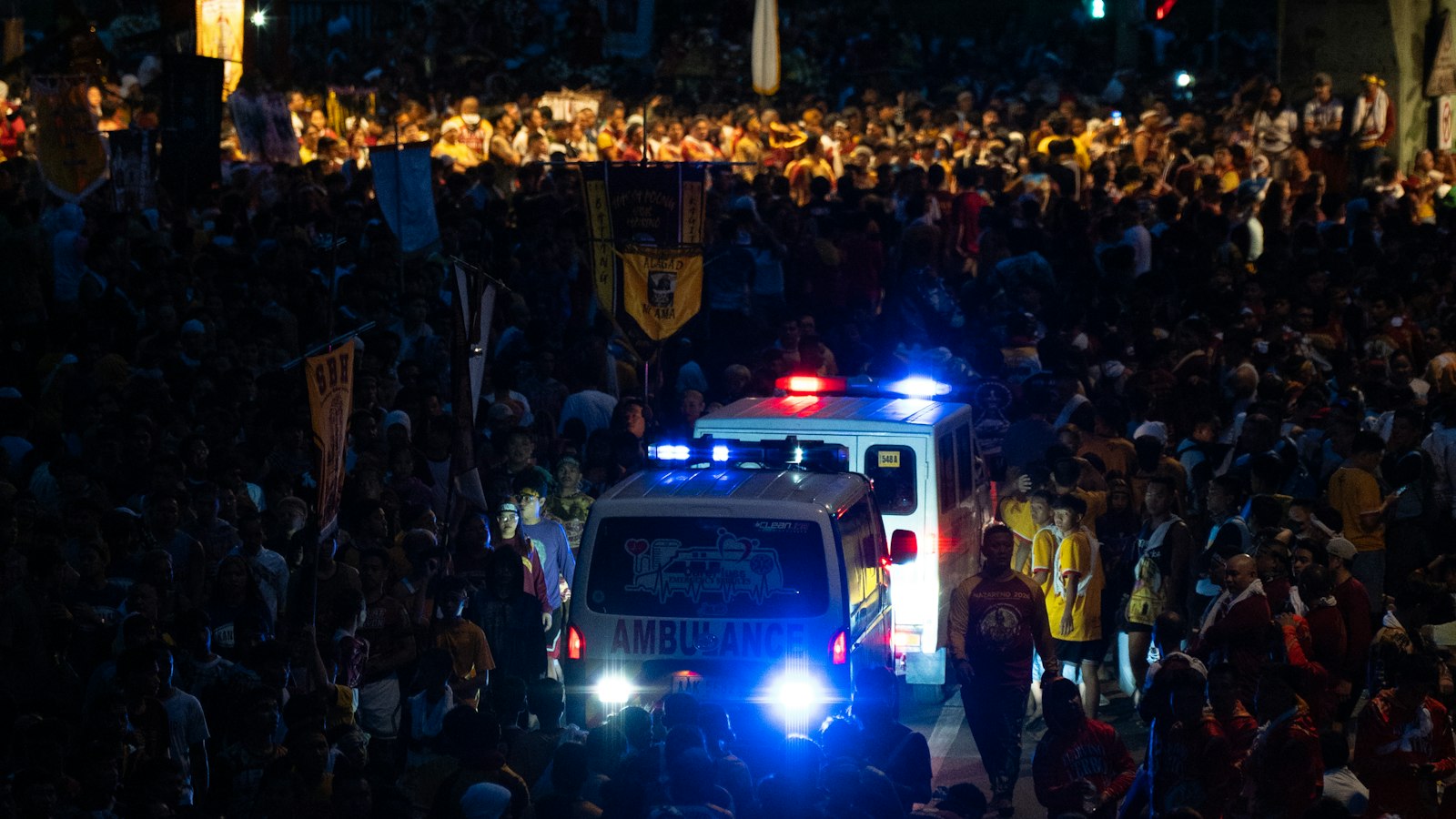 Ambulance with flashing blue lights driving slowly through a dark crowded street