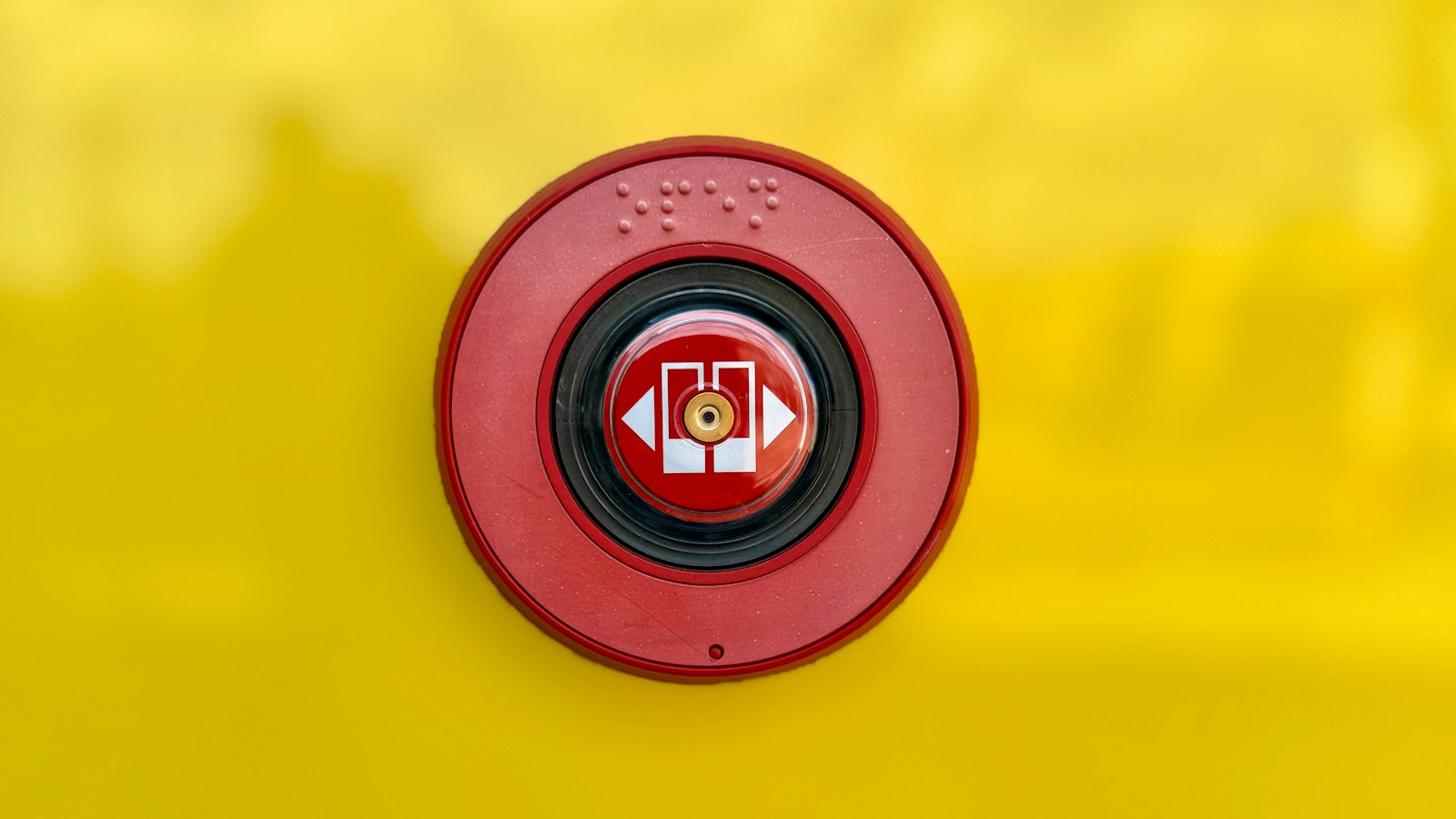 A round red emergency push button set into a bright yellow panel