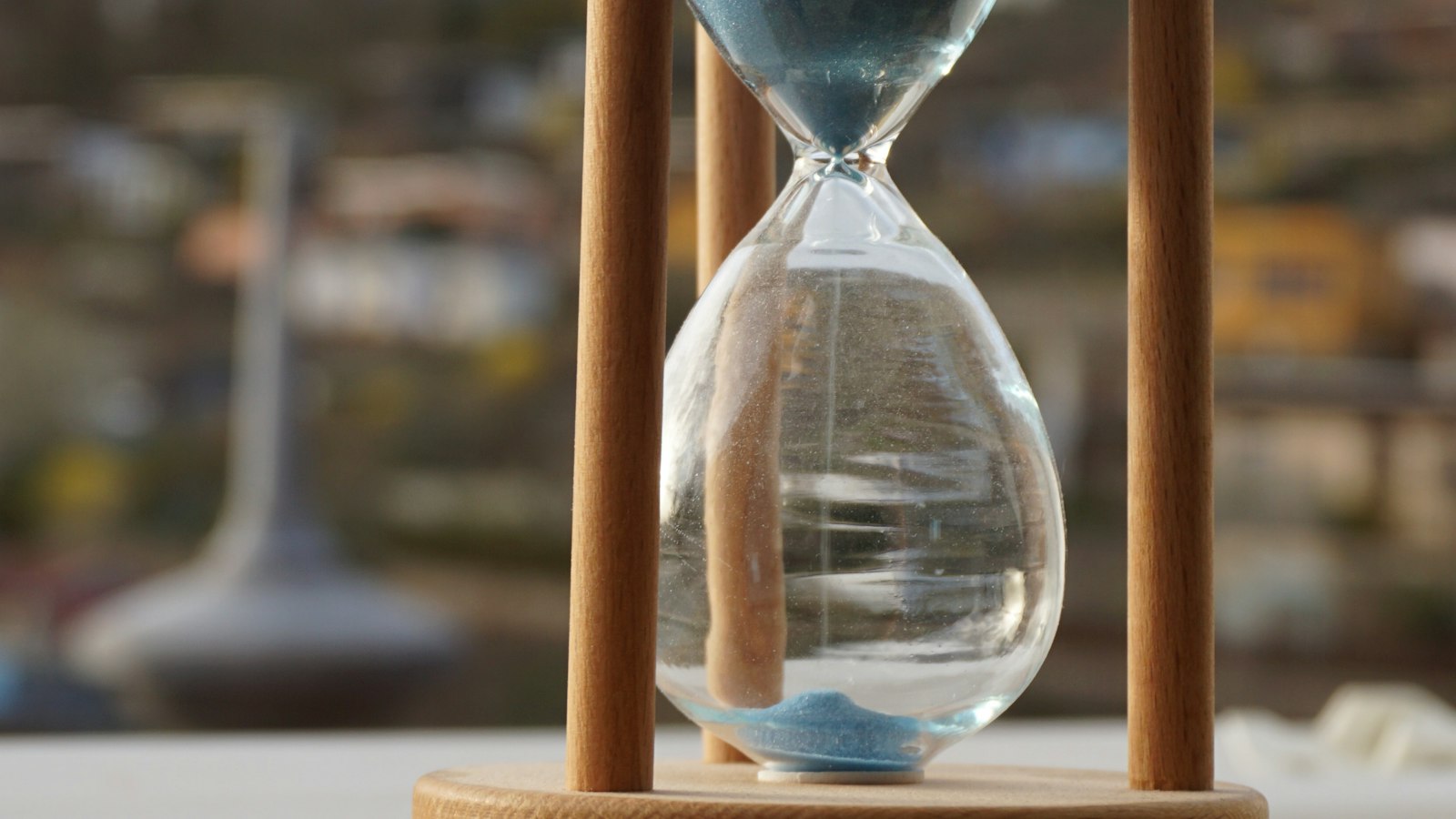 A wooden hourglass with blue sand stands on a table against a blurred background
