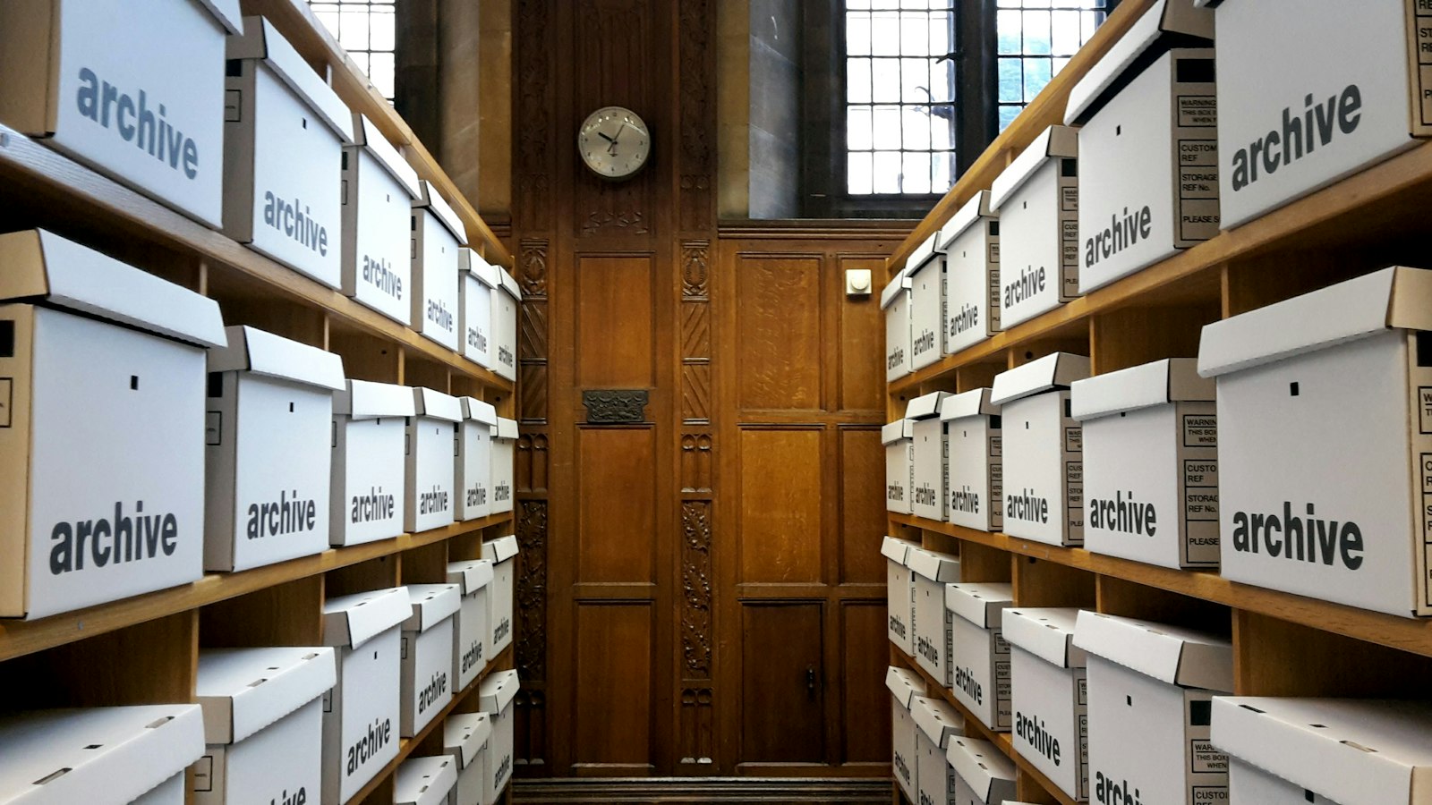 Rows of white archive boxes stacked on wooden shelves in a records room