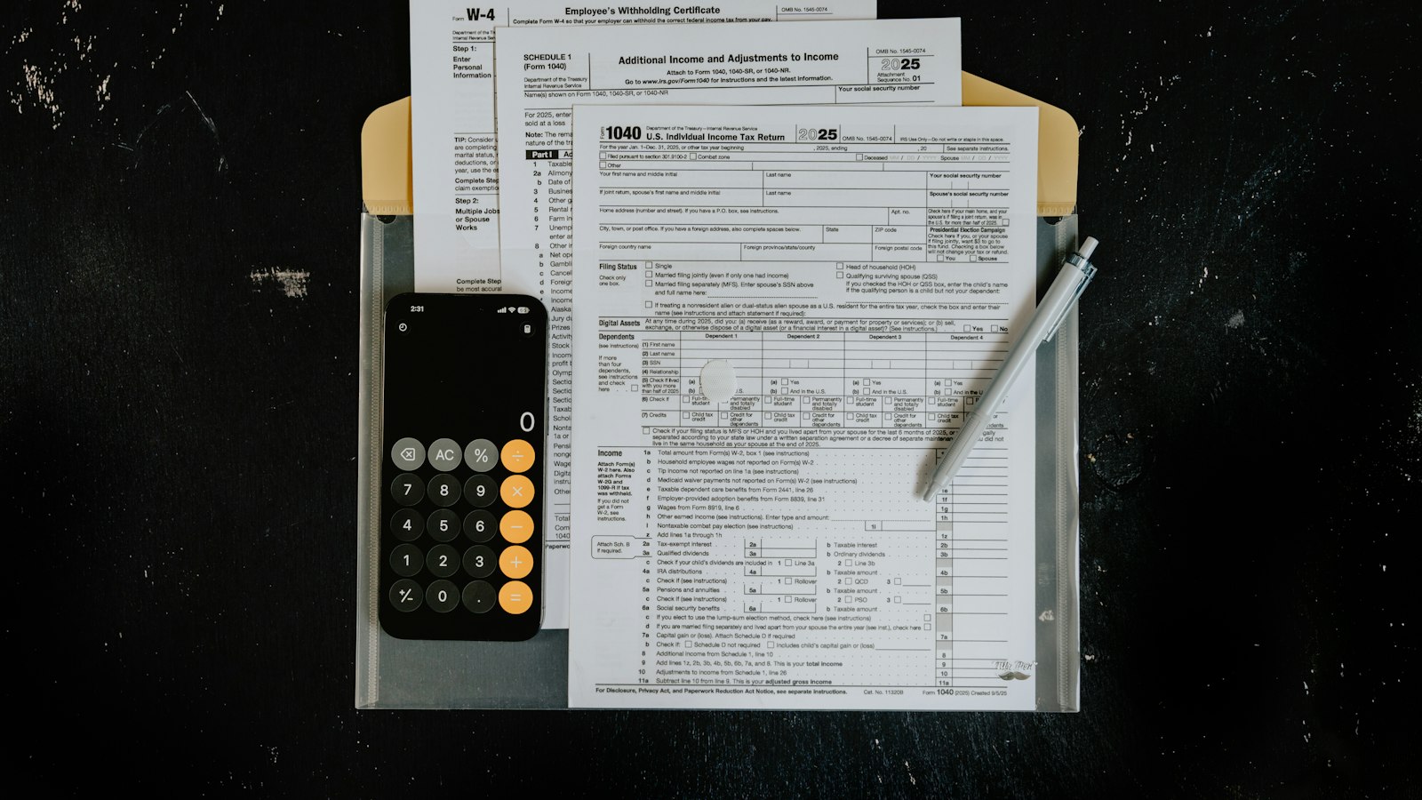 Tax forms, a phone calculator and a pen laid out on a dark surface