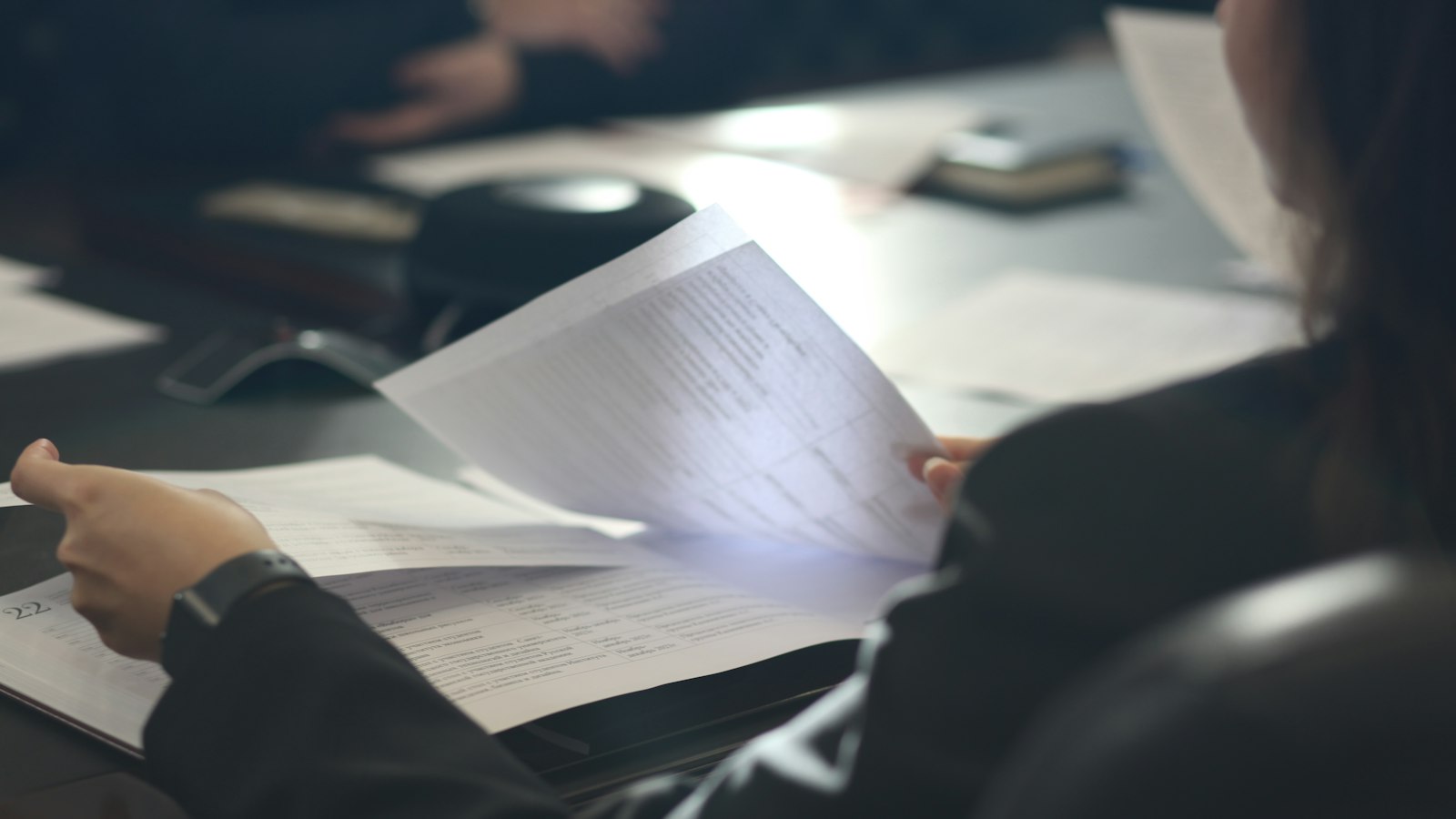 Person in a dark blazer reads printed pages at a conference table
