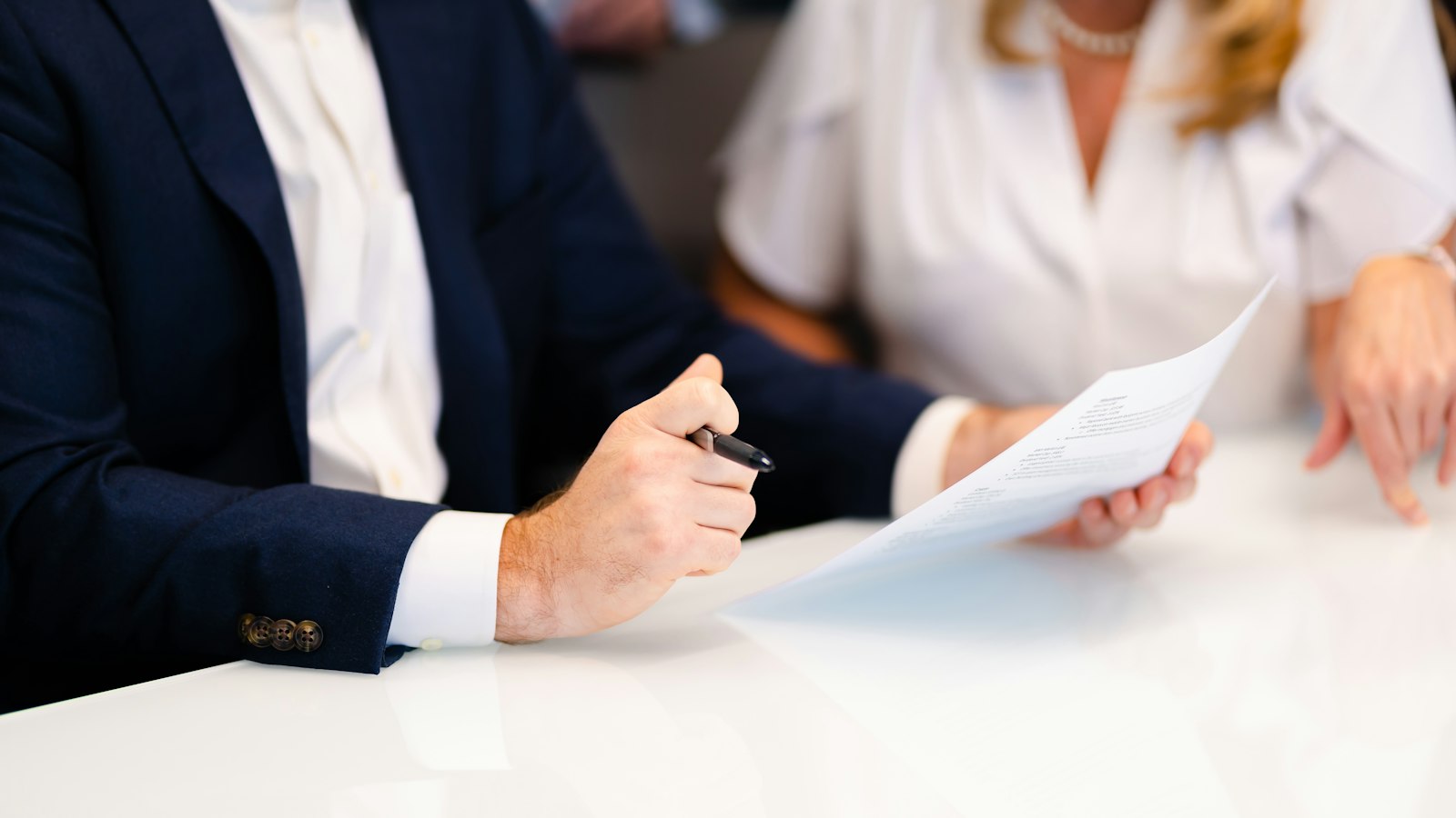 Hands holding a pen and a paper at a white table during a meeting