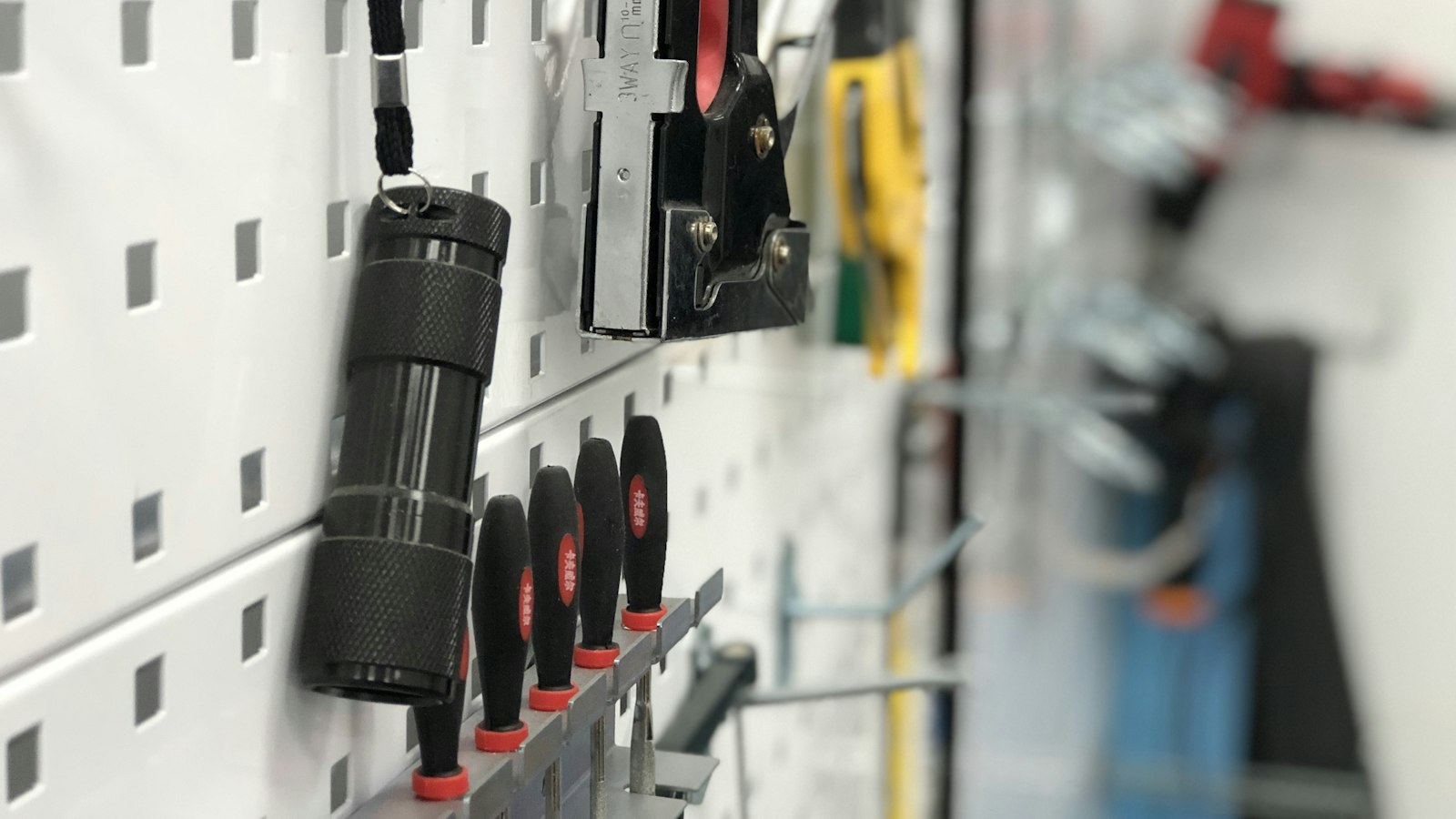 Hand tools and a flashlight hanging neatly on a white perforated pegboard wall