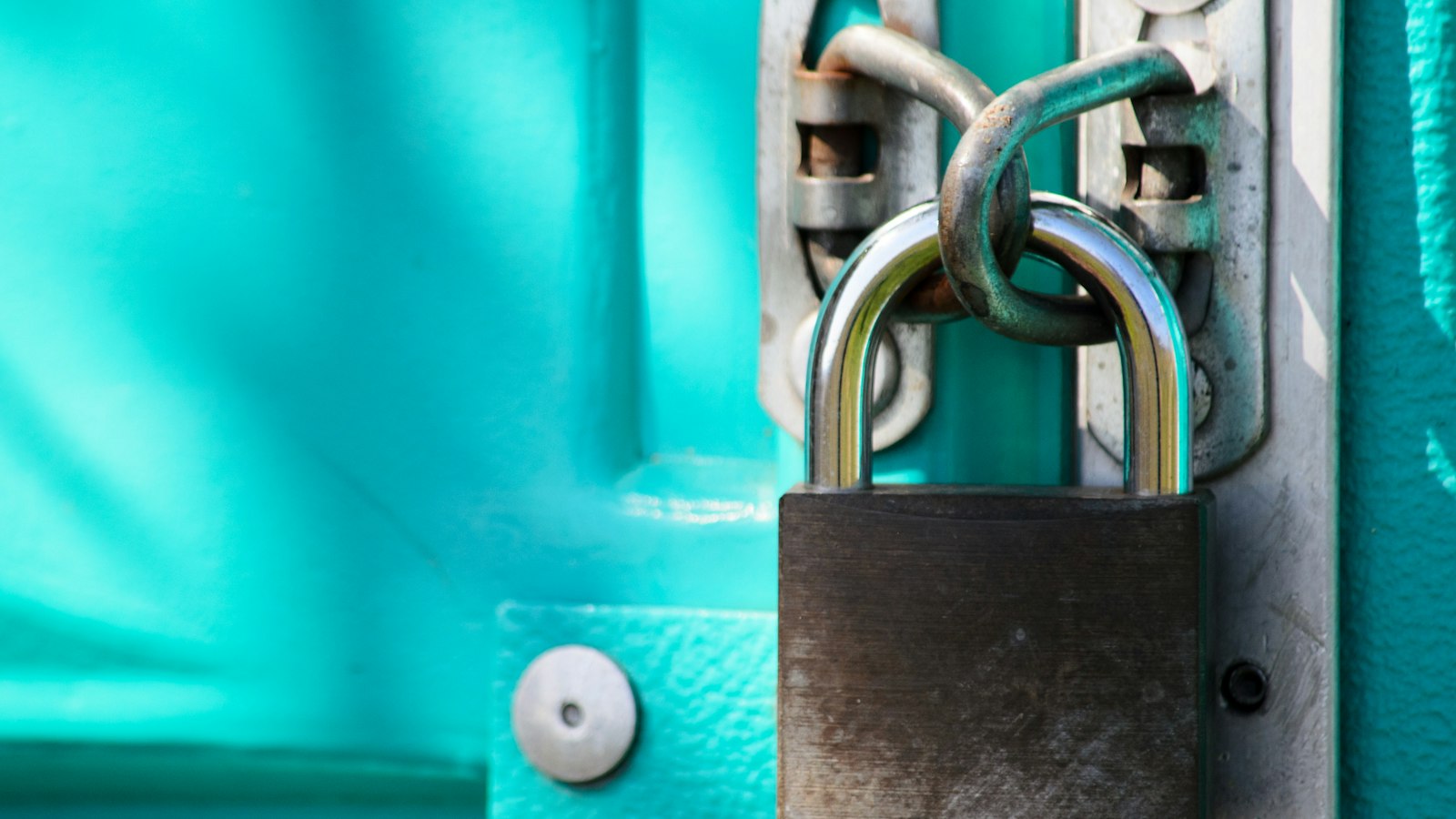 Close-up of a steel padlock securing a latch on a teal door