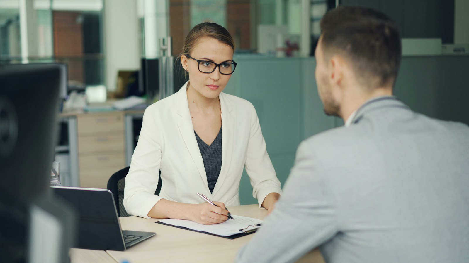 A hiring manager in glasses interviews a candidate at an office desk