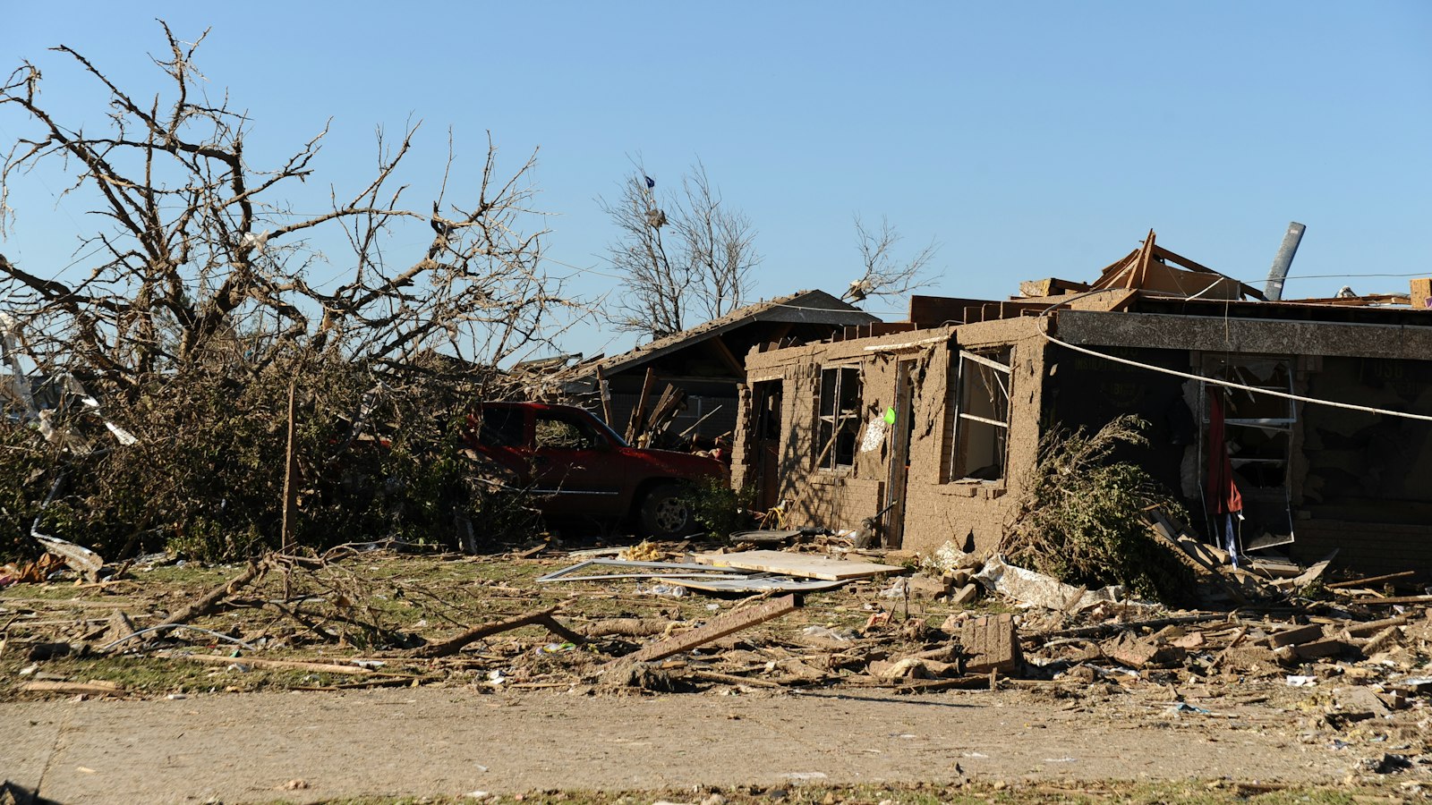 A damaged house with debris and broken trees in the yard after a storm