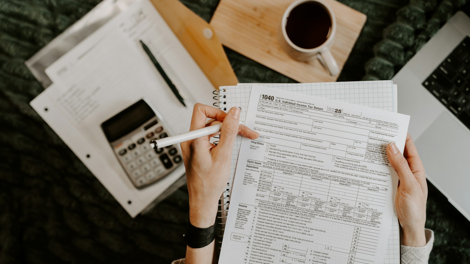 Person's hands filling out a tax form beside a calculator and notebook