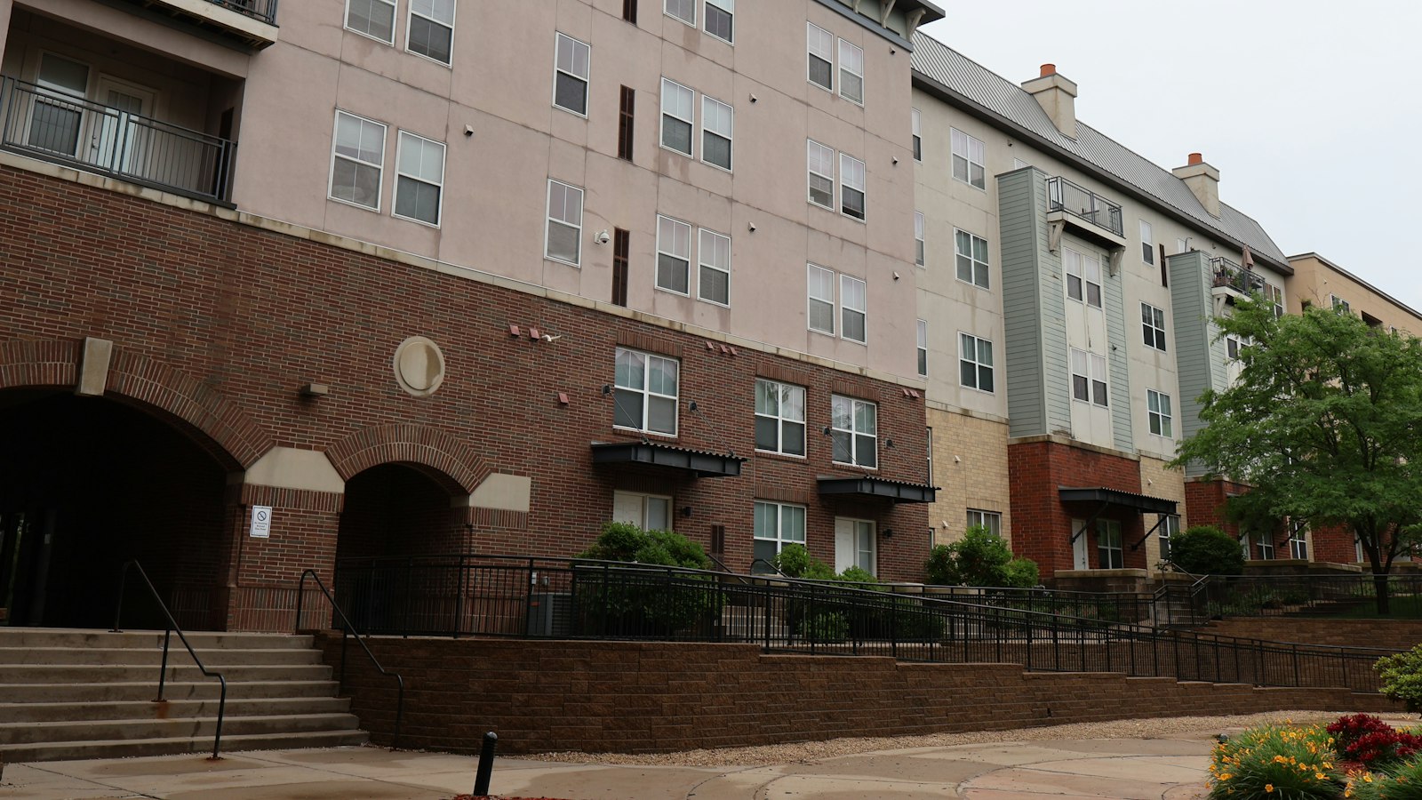 Brick and stucco apartment buildings with entrance stairs and a railing on a sunny day