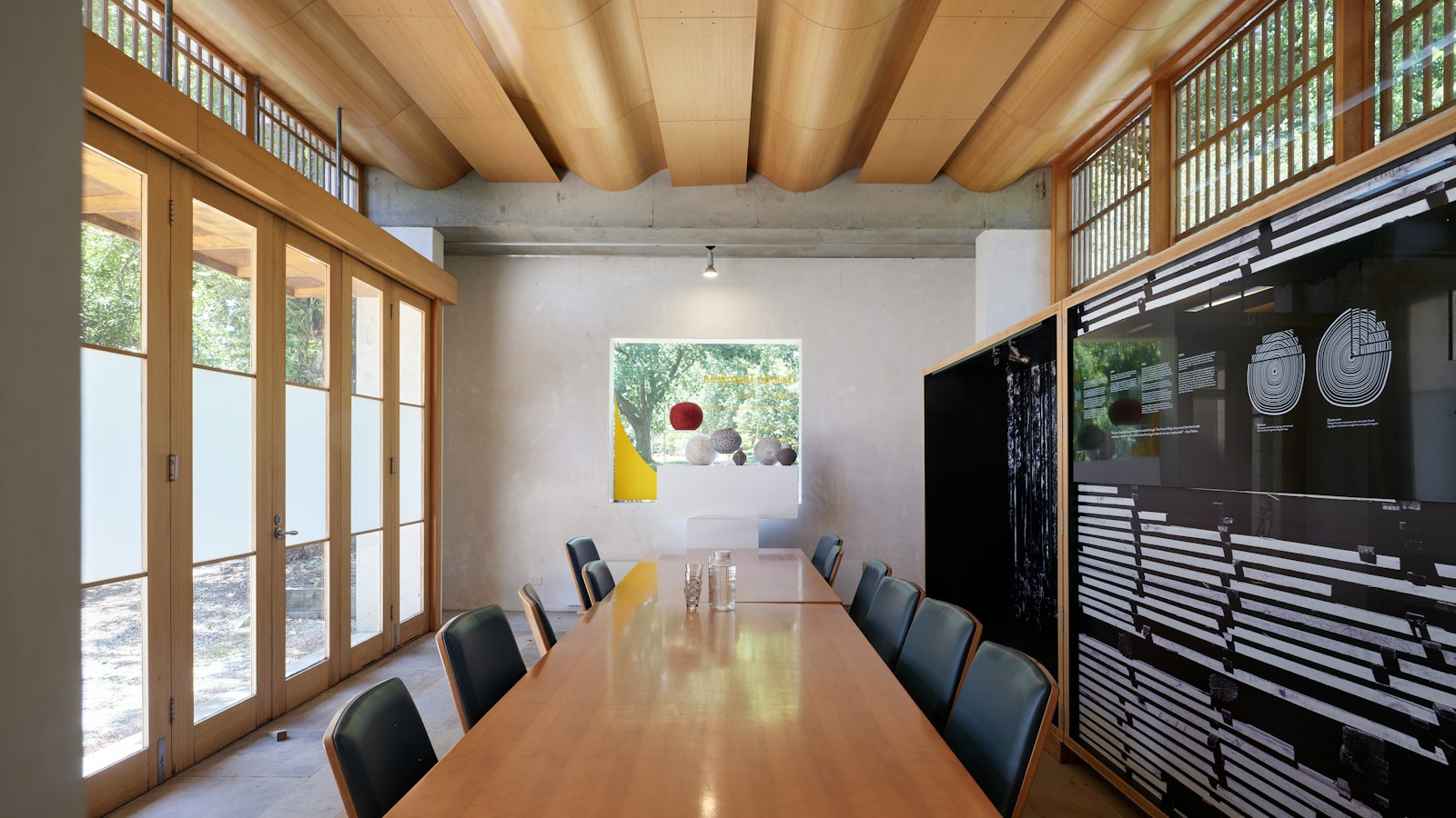 Empty conference room with a long wooden table and dark chairs beside tall windows