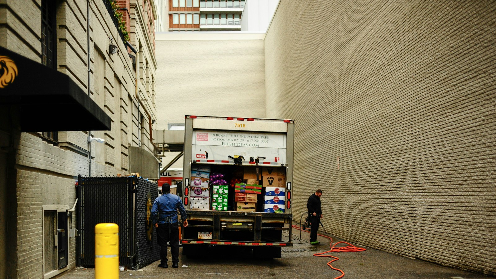 Two workers unload boxes from a delivery truck parked in a narrow city alley