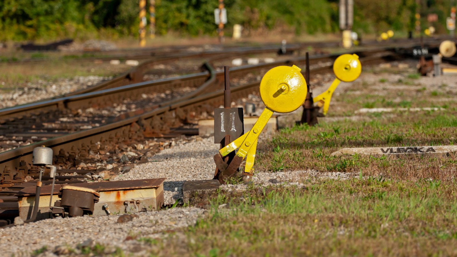 Two yellow railway signal levers beside curving train tracks in daylight