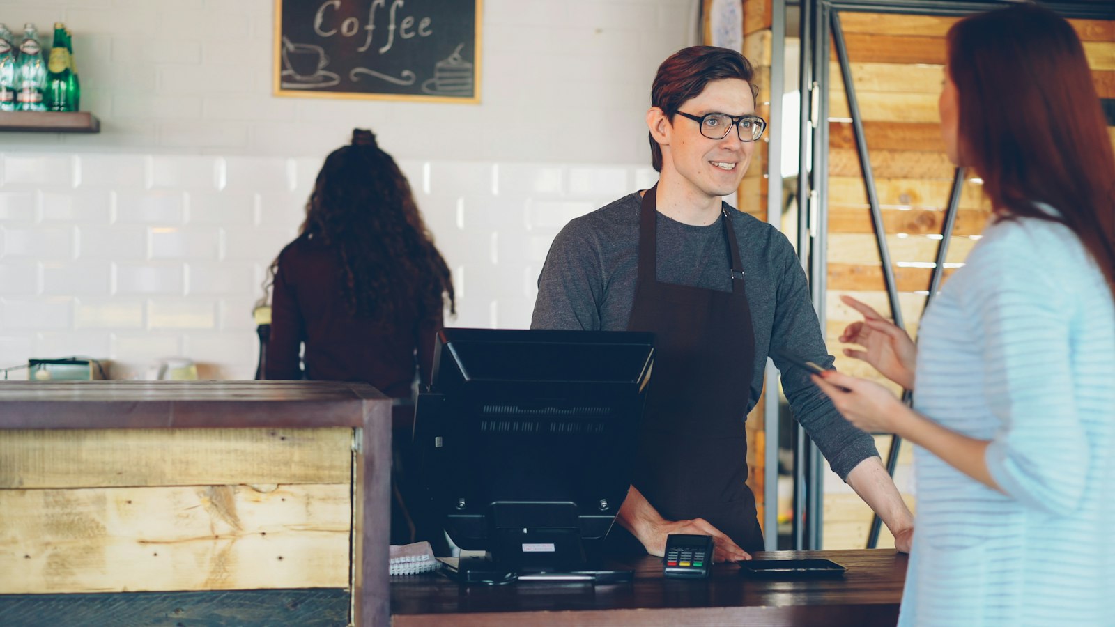 Cashier in an apron talking with a customer at a coffee shop counter