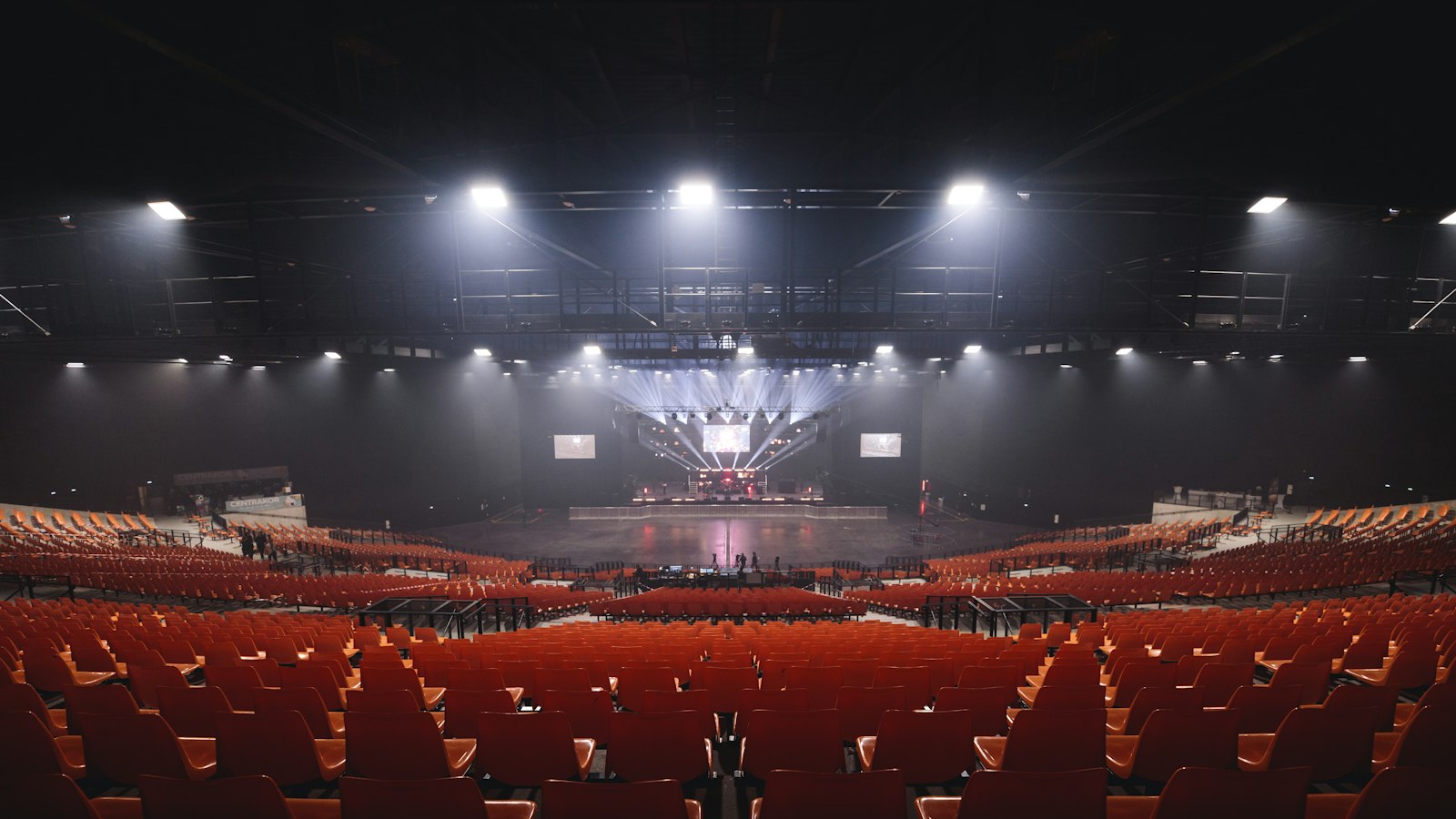 Rows of empty orange seats facing a lit stage in a large dark arena