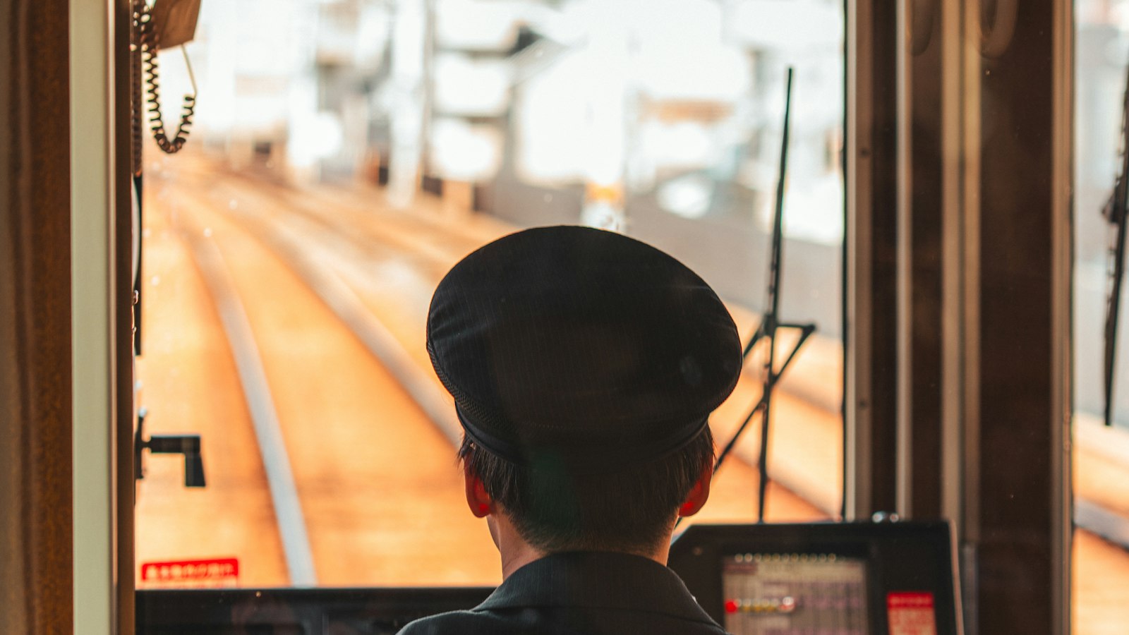 A train driver in a uniform cap seen from behind looking down the tracks