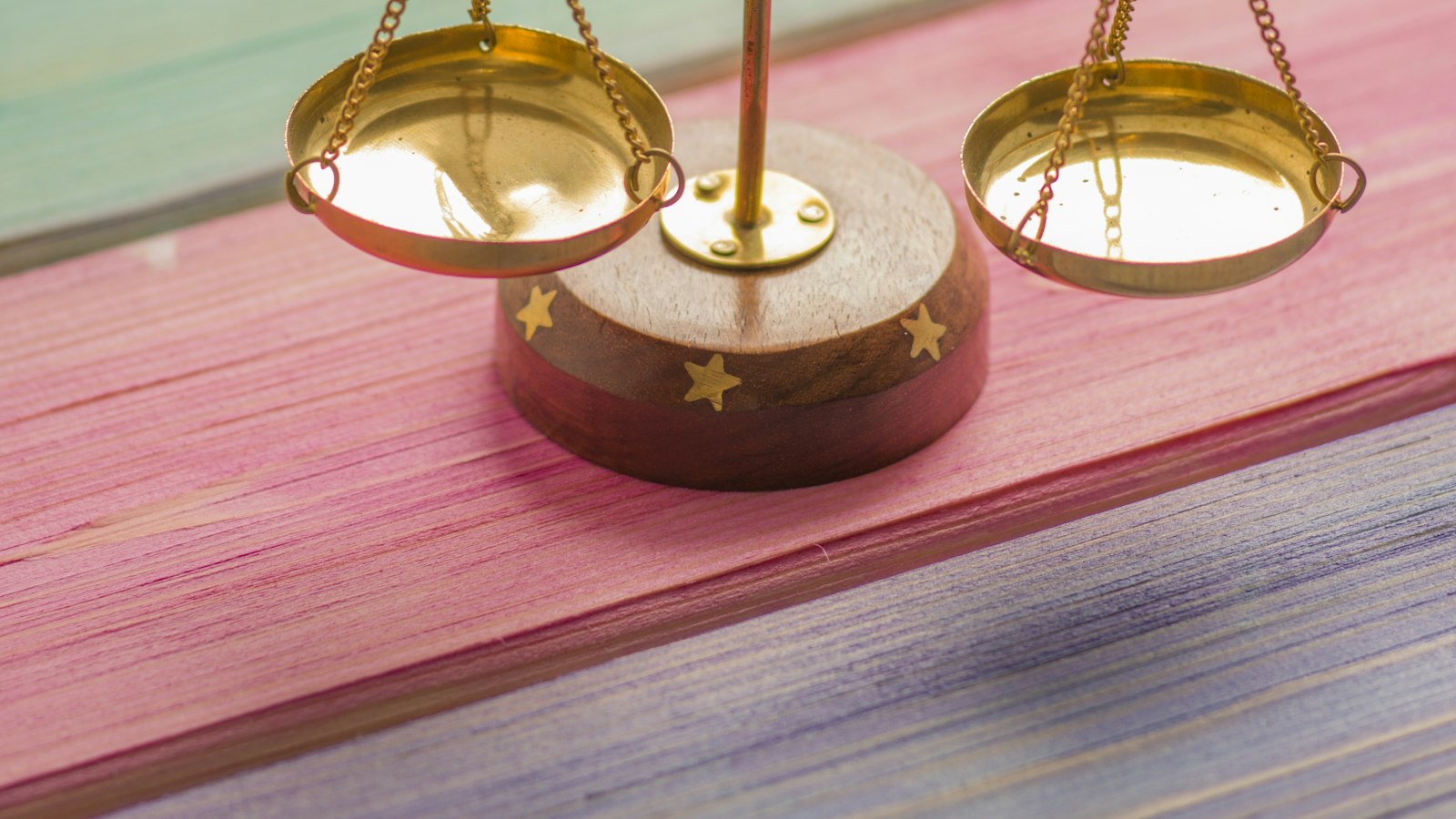 A small gold balance scale with brass pans on a pink and purple wooden surface