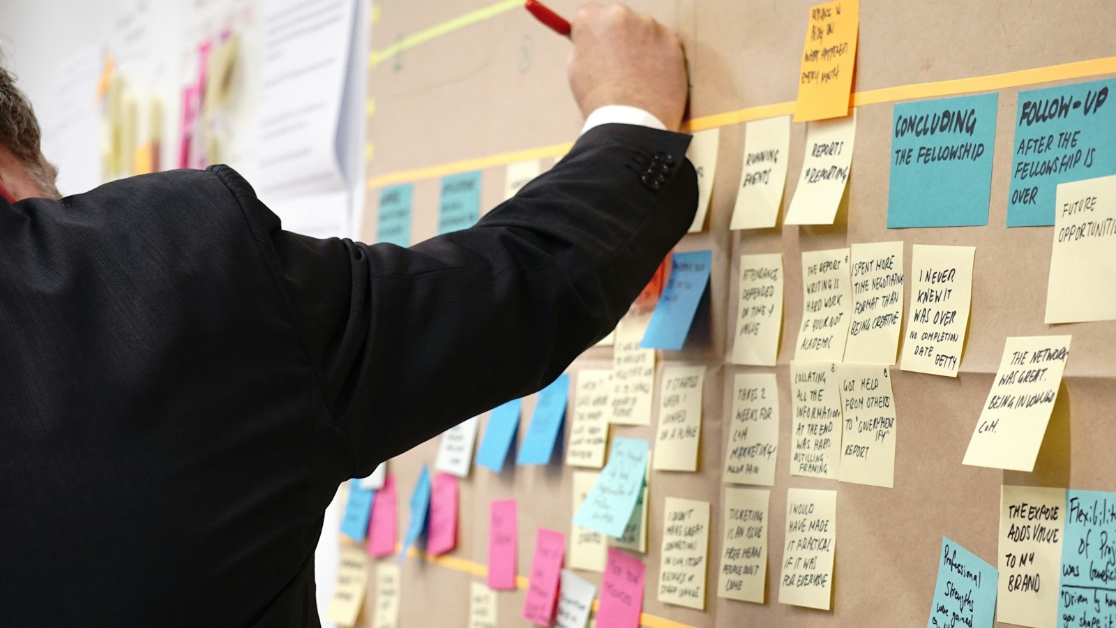 Hand placing a sticky note on a corkboard covered in colorful notes