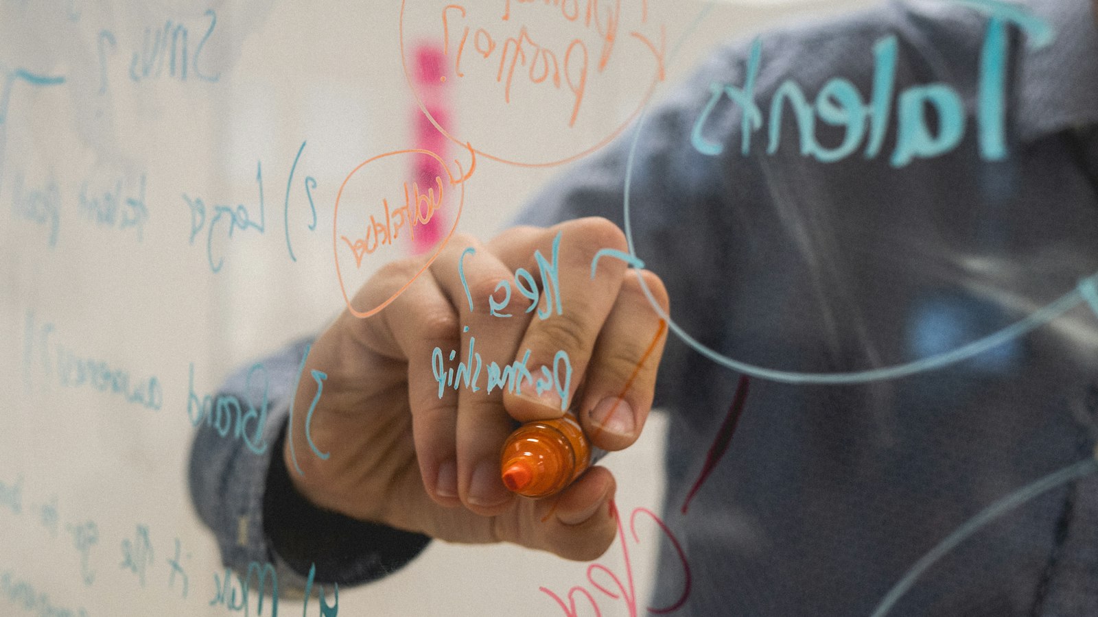 Hand writing with a marker on a glass whiteboard covered in notes