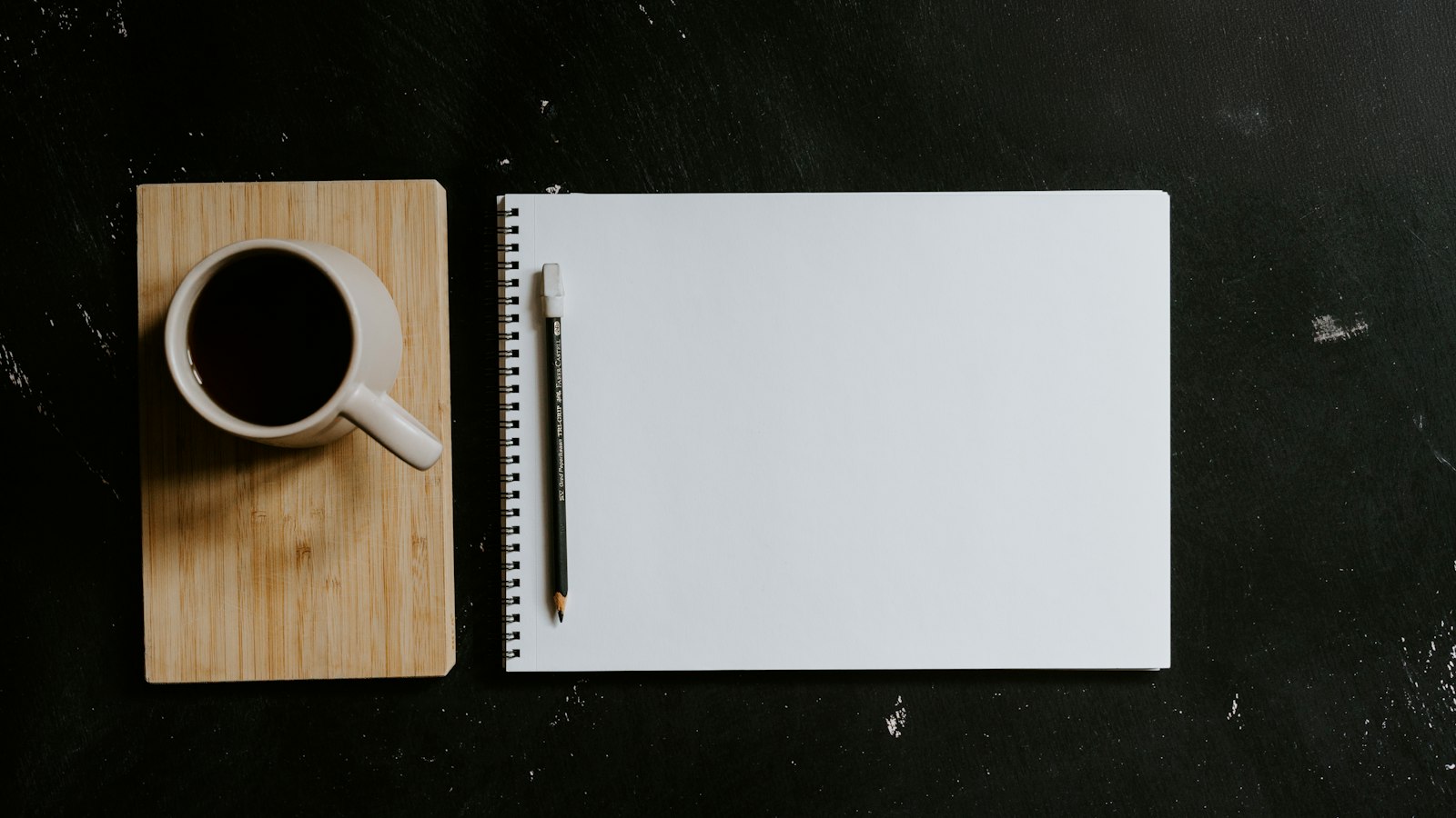 Blank notebook and black coffee mug on a dark desk surface