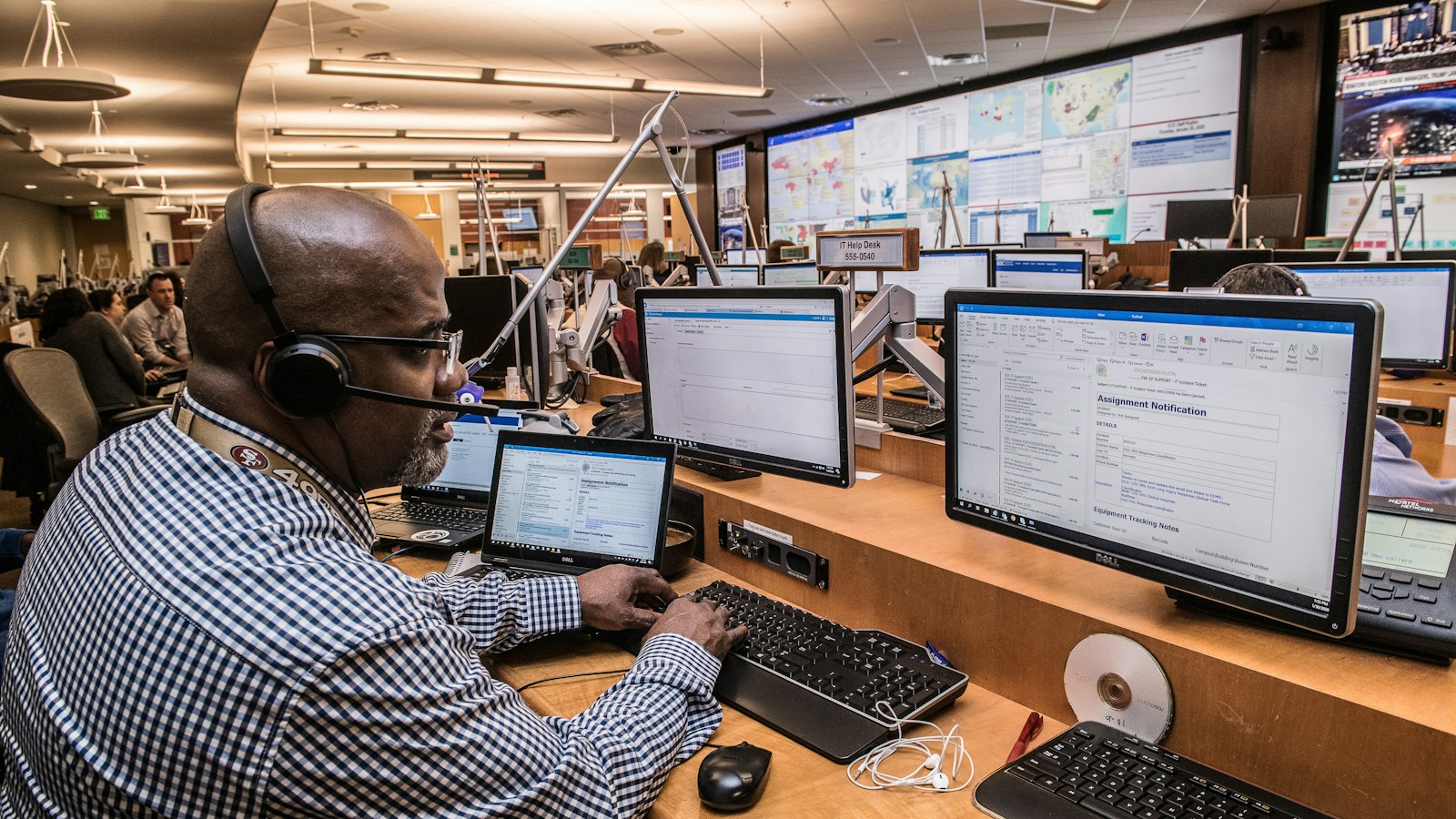 Operator wearing a headset works at computer screens in a busy control center